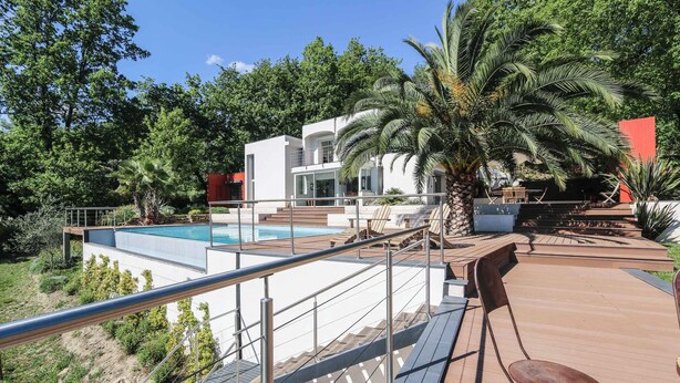 A modern villa with a pool, outdoor seating, and lush greenery.
