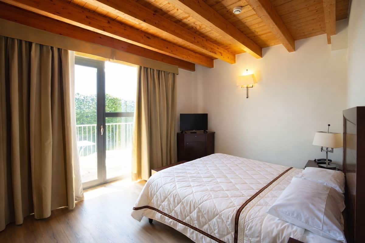 Habitació d'hotel amb un llit gran, televisió, làmpada i un balcó amb cortines.