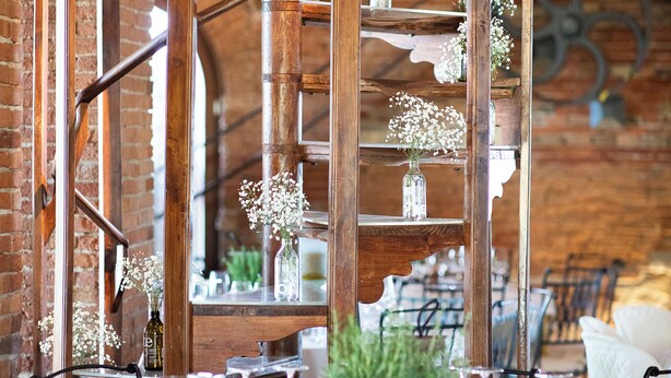 A rustic dining area with exposed brick walls, wooden beams, and a spiral staircase. Tables are set with wine glasses and a centerpiece. - Tenuta Molino dei Sassi (Zevio)