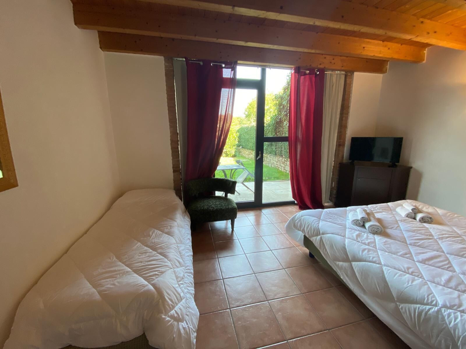 Ein Zimmer mit zwei Betten, einem Sessel, einem Fernseher und Blick ins Freie durch eine Glastür.