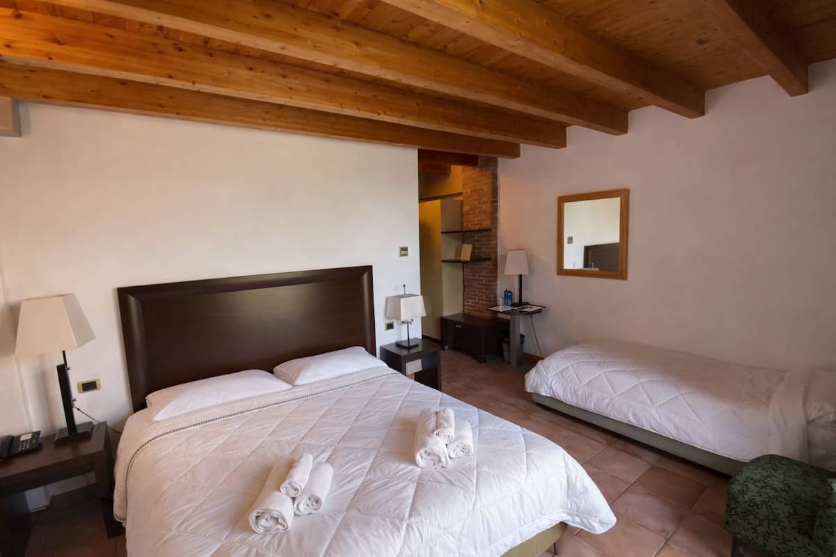 Una habitació d'hotel amb dos llits, un sostre de fusta, una paret de maó, un escriptori petit i un mirall.