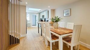 A dining area with a wooden table and white chairs, a potted plant, and a view into the kitchen. - Host Stay Ginger Bread Cottage (Middlesbrough)