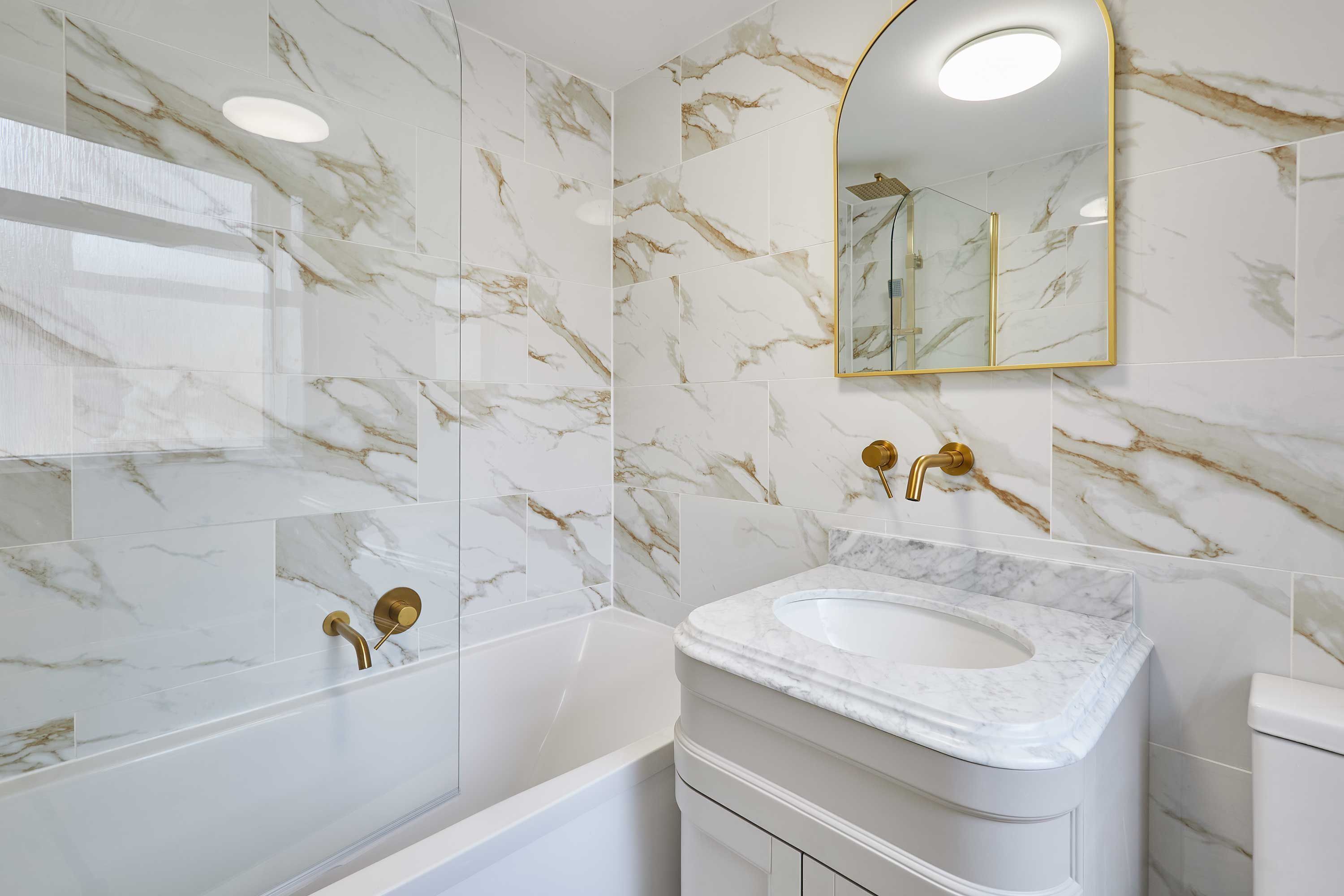 Een badkamer met marmeren tegels, een witte wastafel en een gouden kraan.