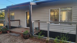 A single-story house with a front porch, a small garden area with potted plants, and a metal railing. - La Maisonnette (Daylesford)