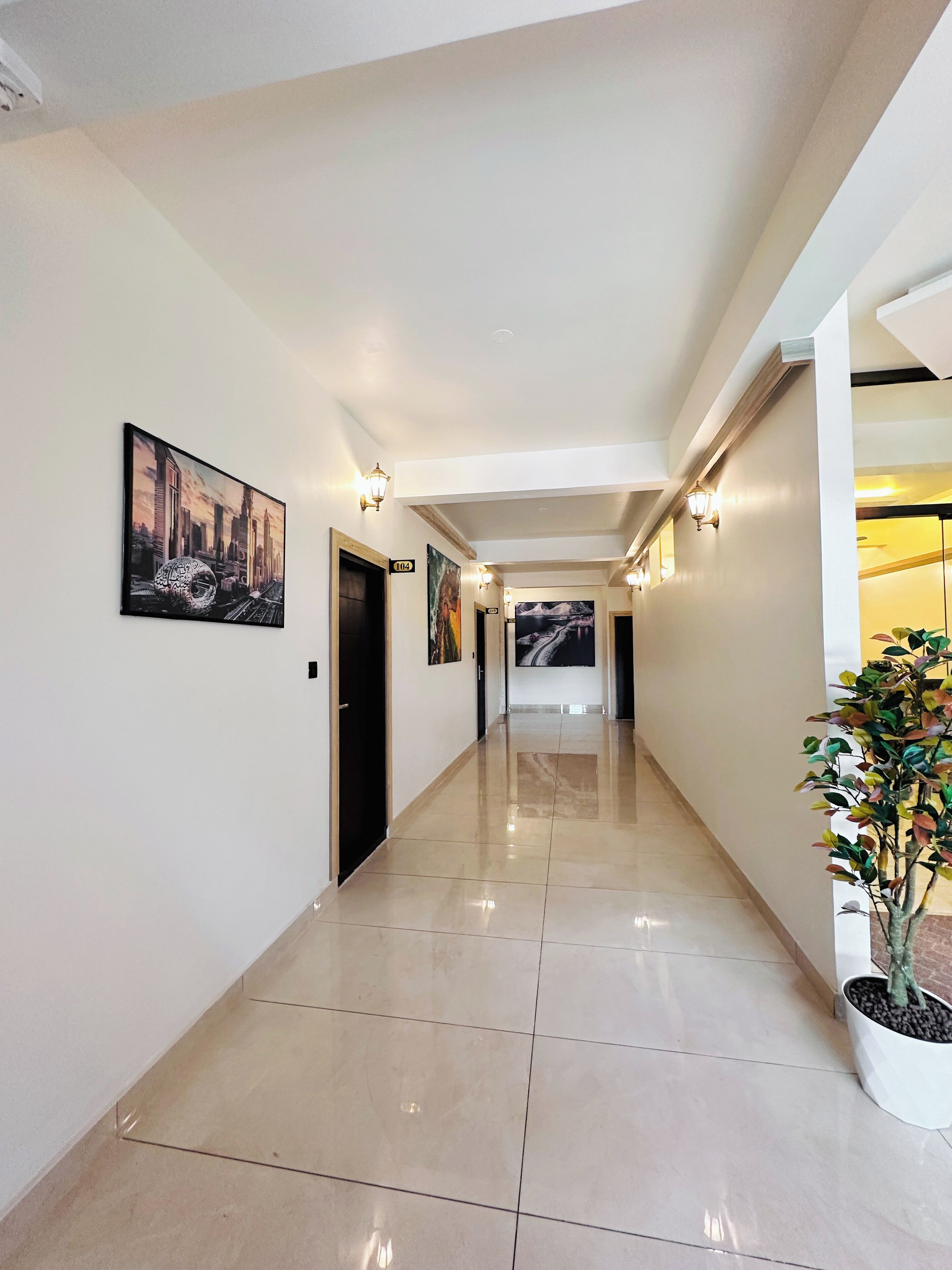 A hallway with a polished floor, wall-mounted artwork, and a potted plant.