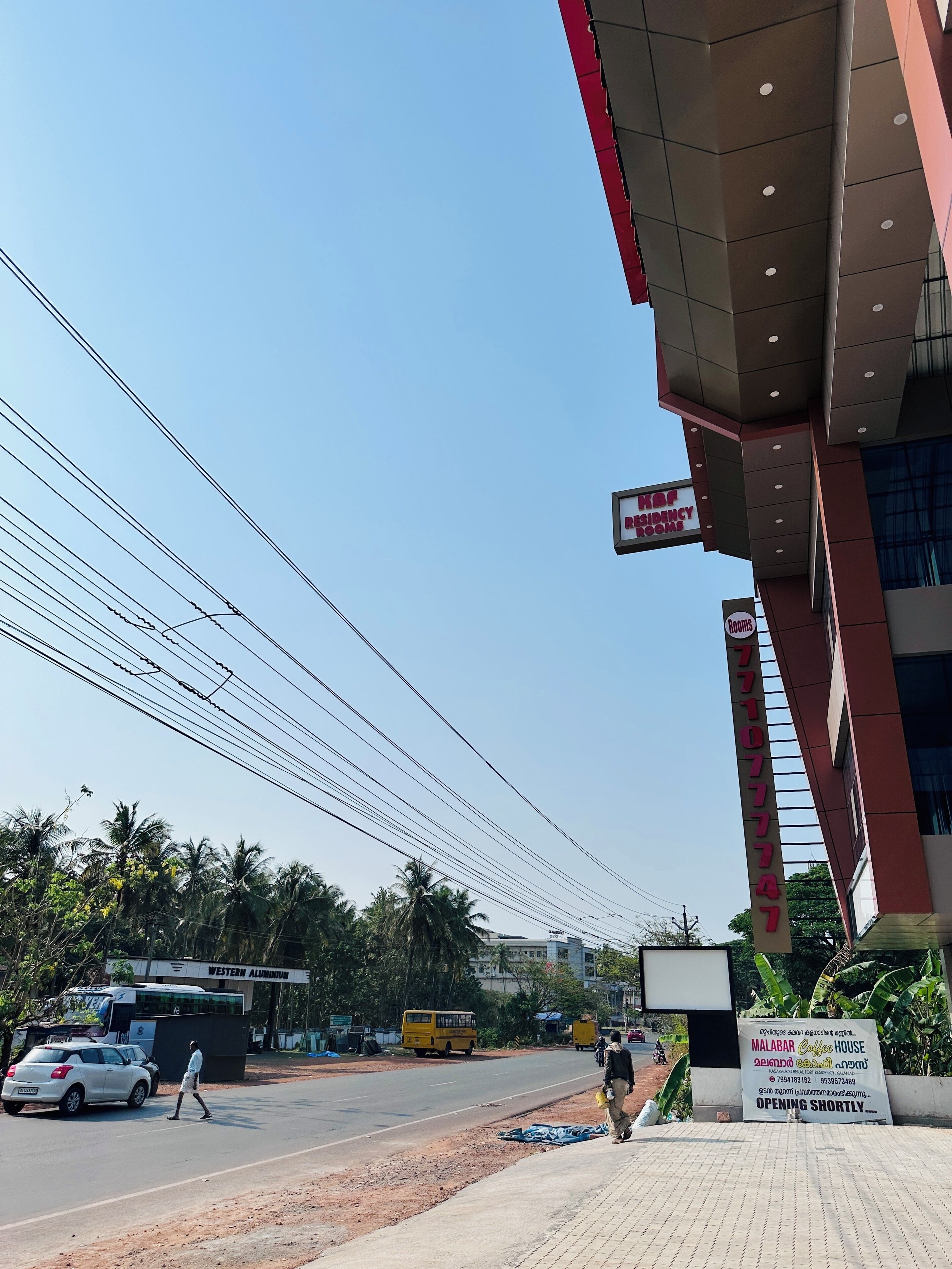 A hotel with a sign indicating 'Kop Residency Rooms' and a sign for 'Malabar Coffee House' with a note about opening shortly.