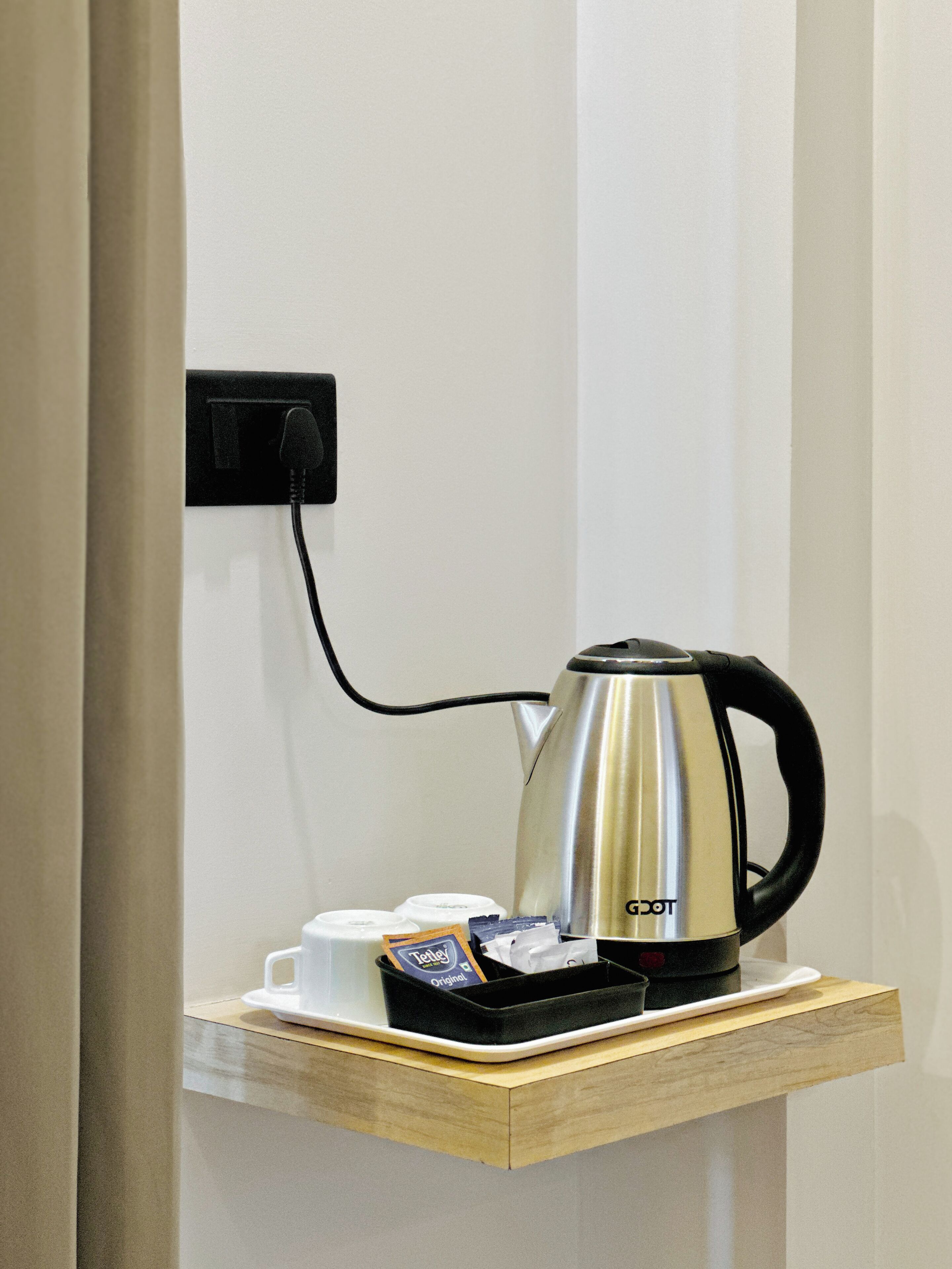 A kettle on a wooden shelf, a coffee cup, and a box of tea bags.