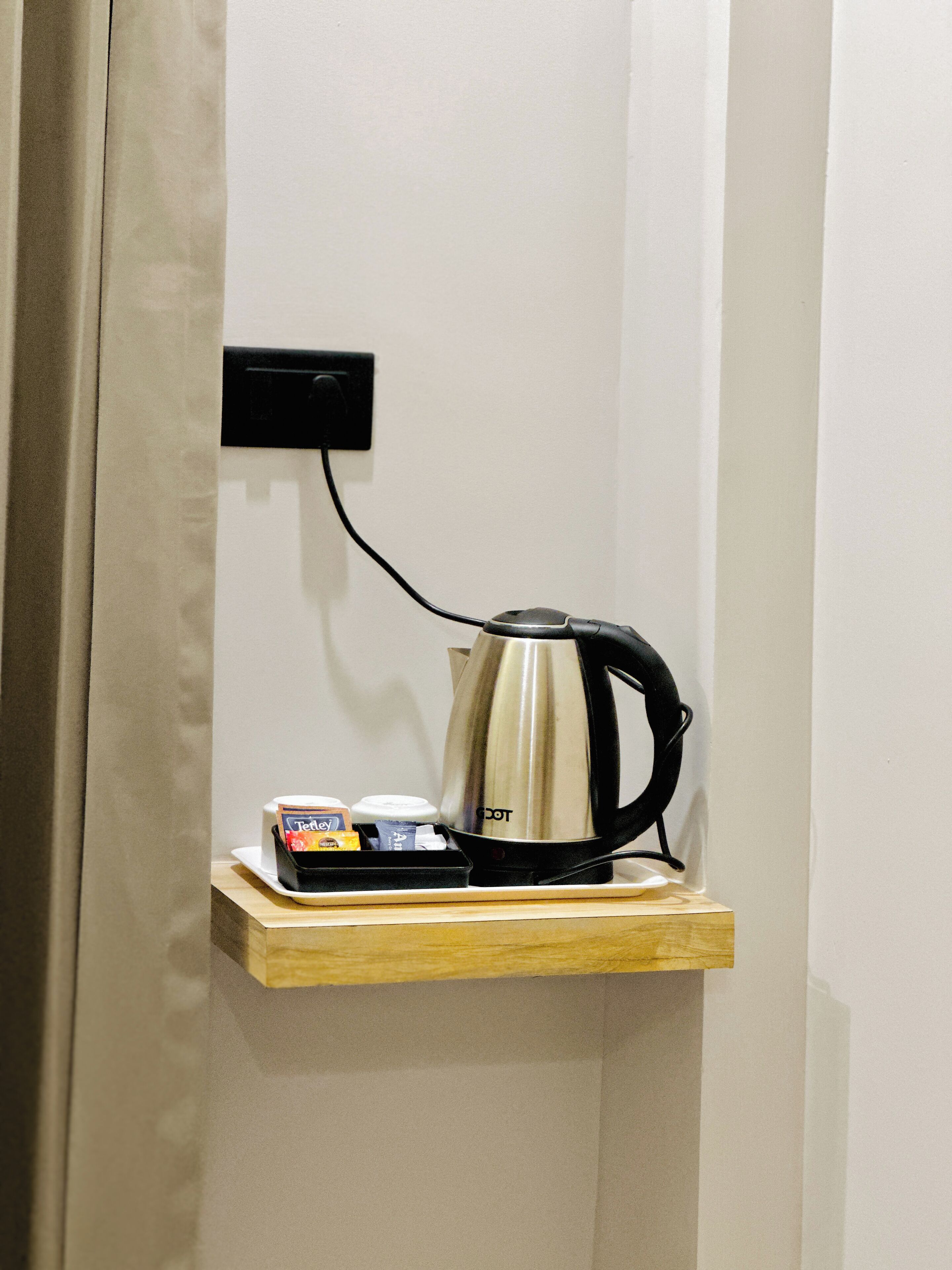 A kettle on a wooden shelf with a power outlet above it.
