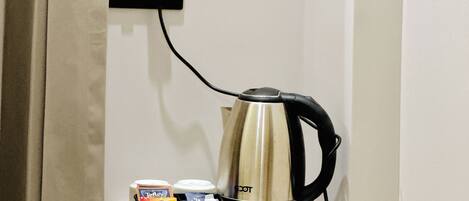 A kettle on a wooden shelf with a power outlet above it.