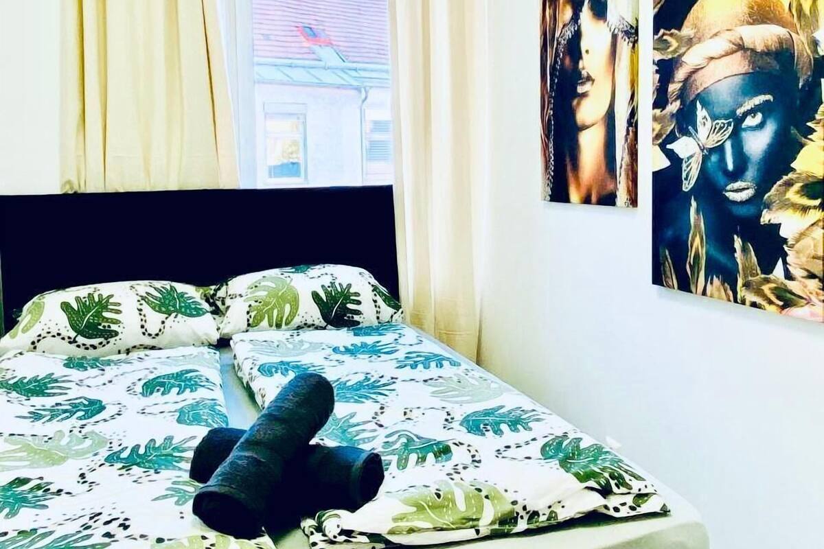 Un dormitorio con cama, cortinas, una ventana y dos obras de arte en las paredes.
