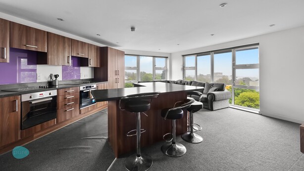 A modern kitchen with a central island, bar stools, and large windows offering a view of the city. - 8 Bed Apartment @ Derriford Stays by Pureserviced (Plymouth)