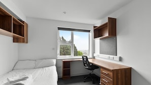 A bedroom with a bed, a desk with a chair, a window, and built-in shelving. - 5 Bed Apartment @ Derriford Stays by Pureserviced (Plymouth)