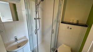 Een badkamer met een douchecabine van glas, een wastafel en een toilet.