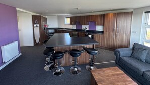 Een moderne keuken met een centraal eiland, barstoelen en een grijze bank.