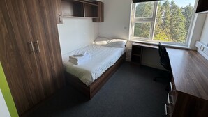Een kleine kamer met een bed, bureau en kledingkast.