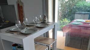 Una cocina compacta con zona de comedor. Incluye una encimera blanca, una mesa de madera y un separador de vidrio.