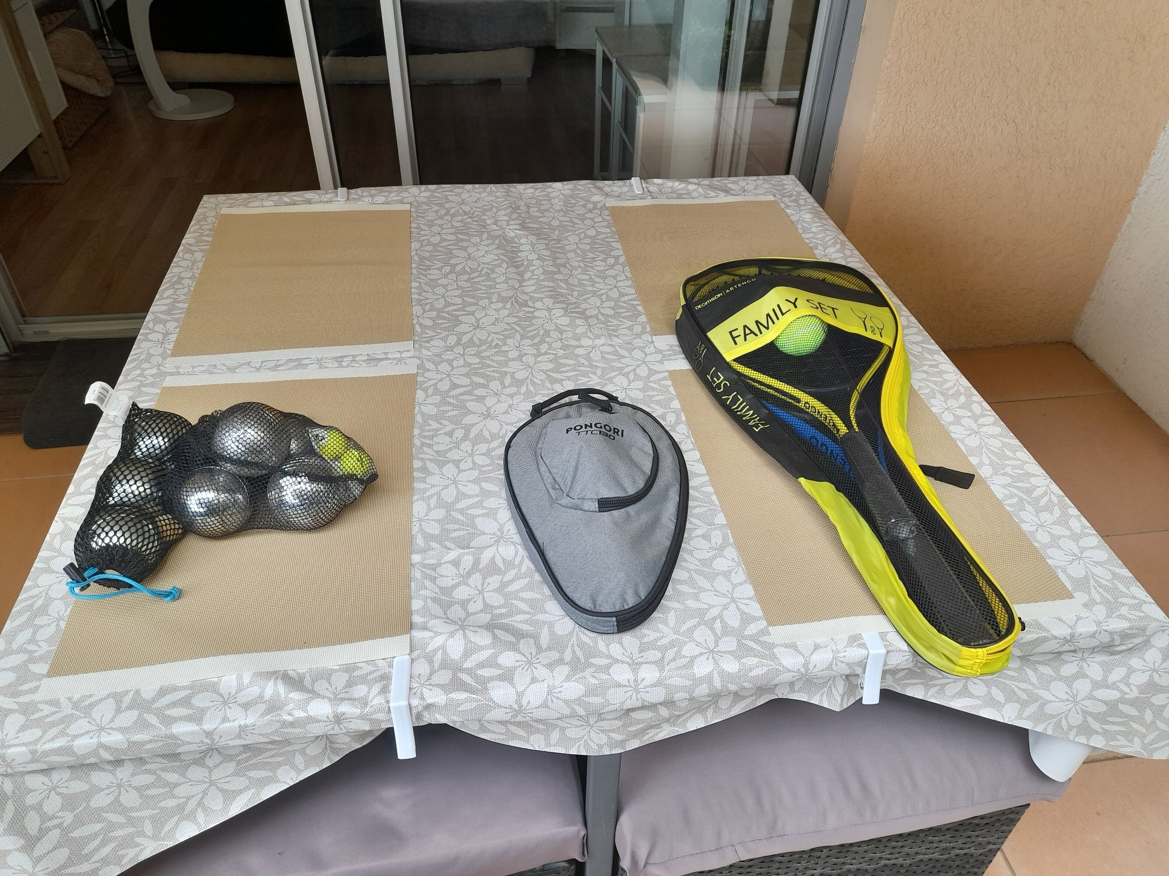 Una mesa con mantel estampado, una bolsa de malla negra, una gorra gris y una botella de agua amarilla y negra.