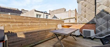 Terraza en la azotea con cubierta de madera, una mesa y unidades de aire acondicionado.
