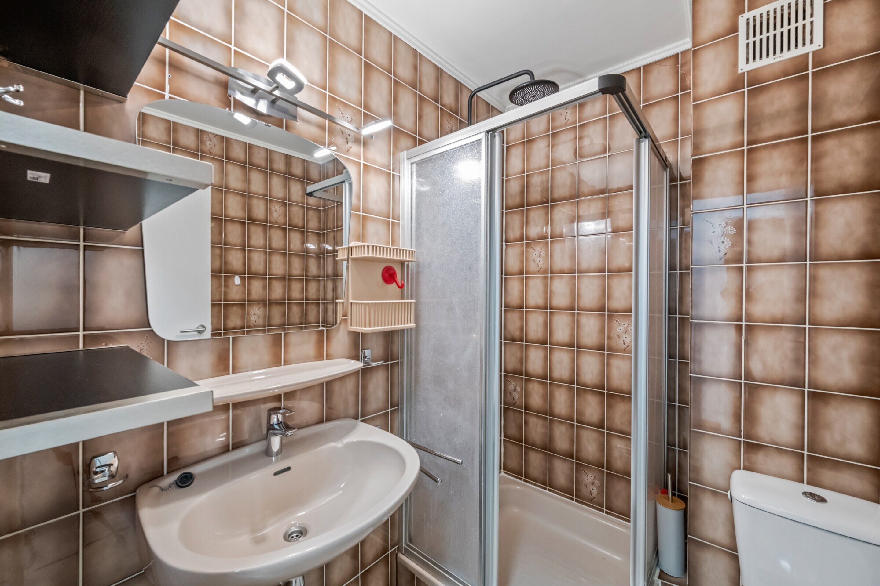 A bathroom with a sink, mirror, shower, and tiled walls.
