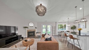En moderne stue med et stort fladskærms-tv, pejs, sofa og et spiseområde med barstole.