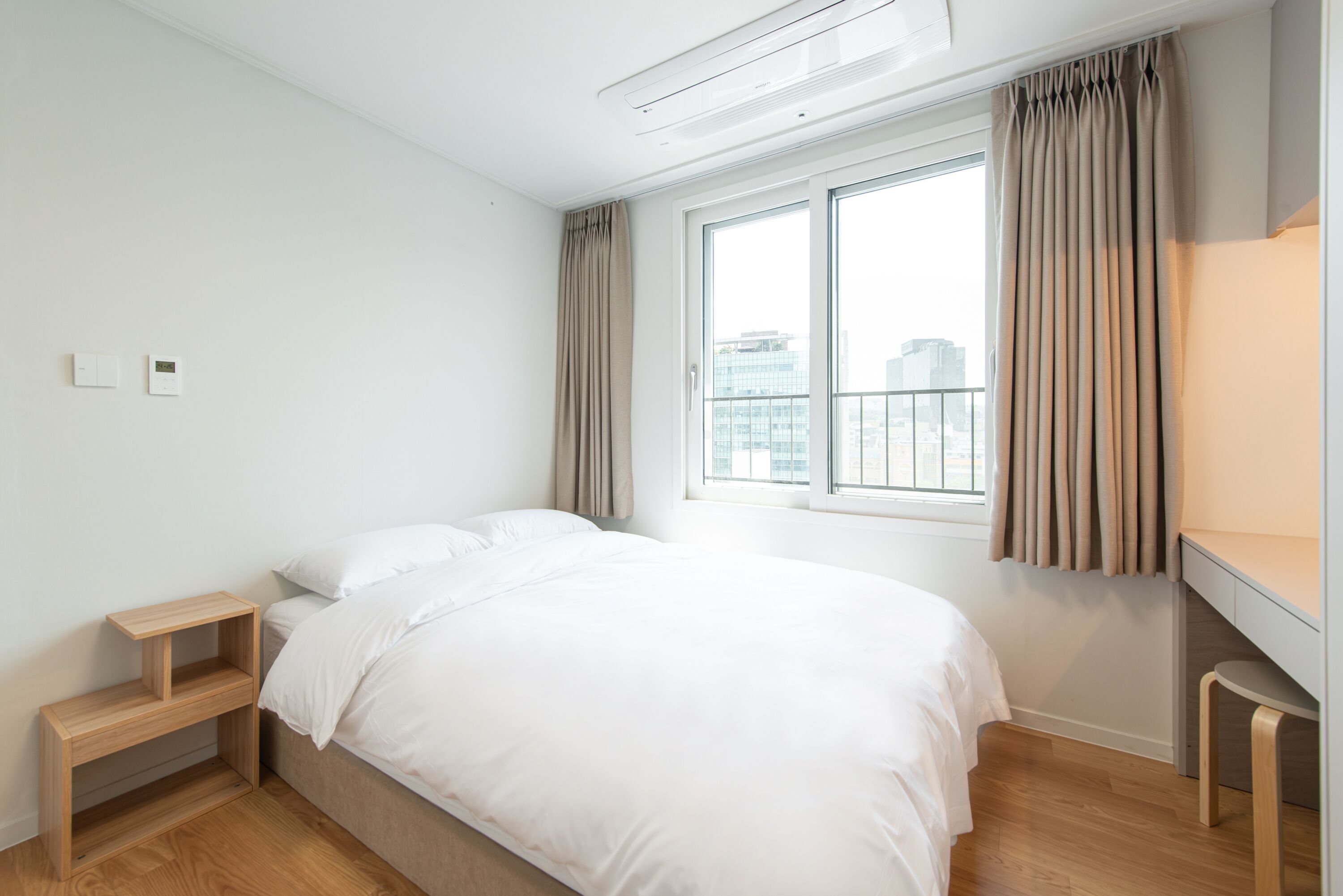 Een moderne slaapkamer met een bed, een nachtkastje, een bureau en een raam met gordijnen.