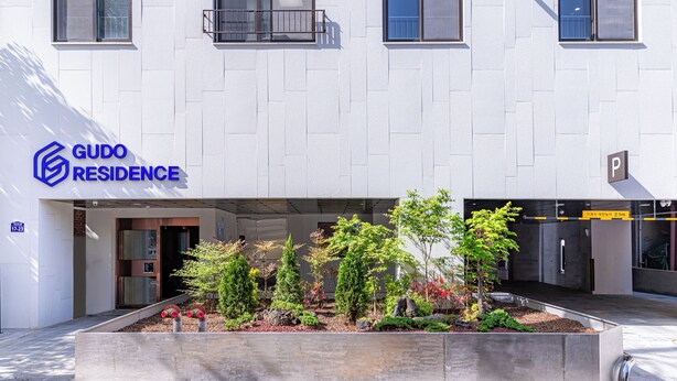 A modern building with a GUDO RESIDENCE sign, a parking entrance, and a landscaped garden area. - GUDO RESIDENCE CHUNGMURO (Seoul)