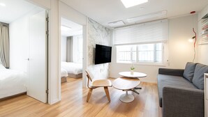 A modern hotel room with a wooden floor, a grey sofa, a round table, and a TV mounted on the wall. - GUDO RESIDENCE CHUNGMURO (Seoul)