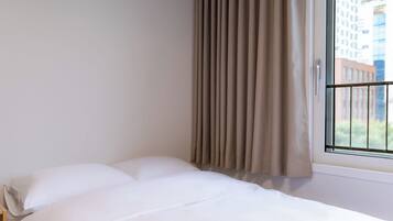 A hotel room with a bed, beige curtains, and a window with a view of buildings.
