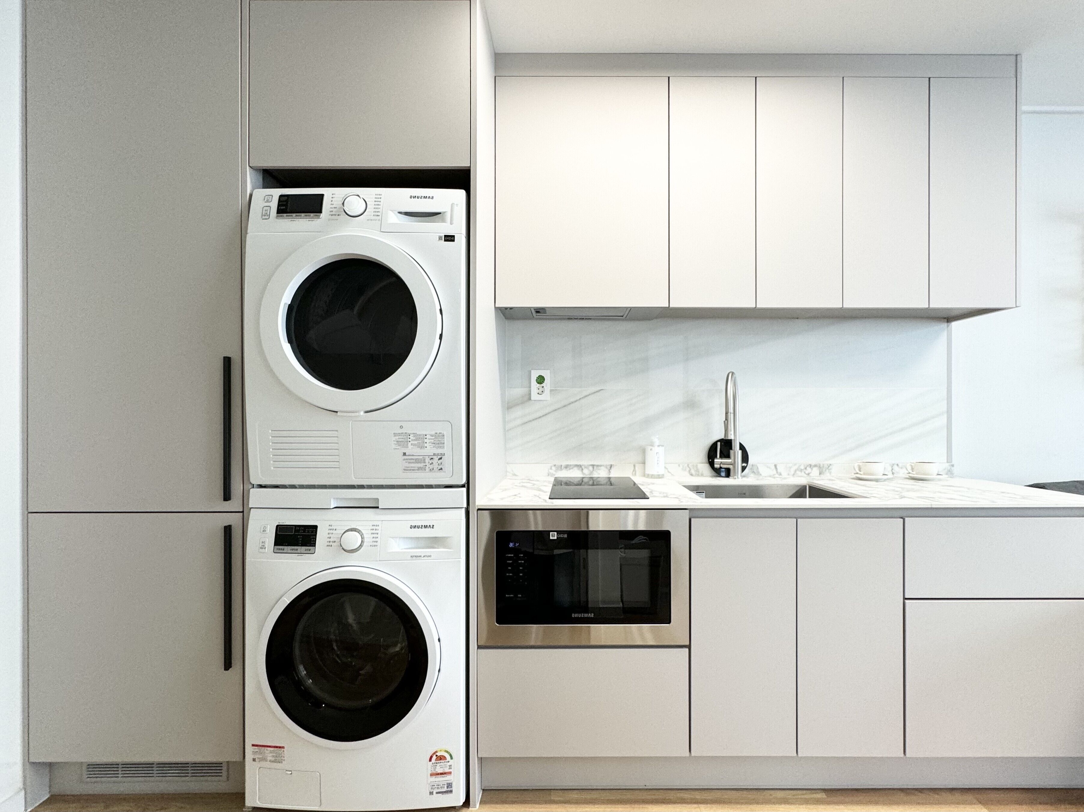 A modern kitchen with a stacked washer and dryer, stainless steel appliances, and a marble backsplash.