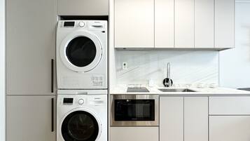 A modern kitchen with a stacked washer and dryer, stainless steel appliances, and a marble backsplash.