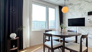 A modern dining area with a round table and four chairs, a TV mounted on the wall, and a window with curtains. - GUDO RESIDENCE CHUNGMURO (Seoul)