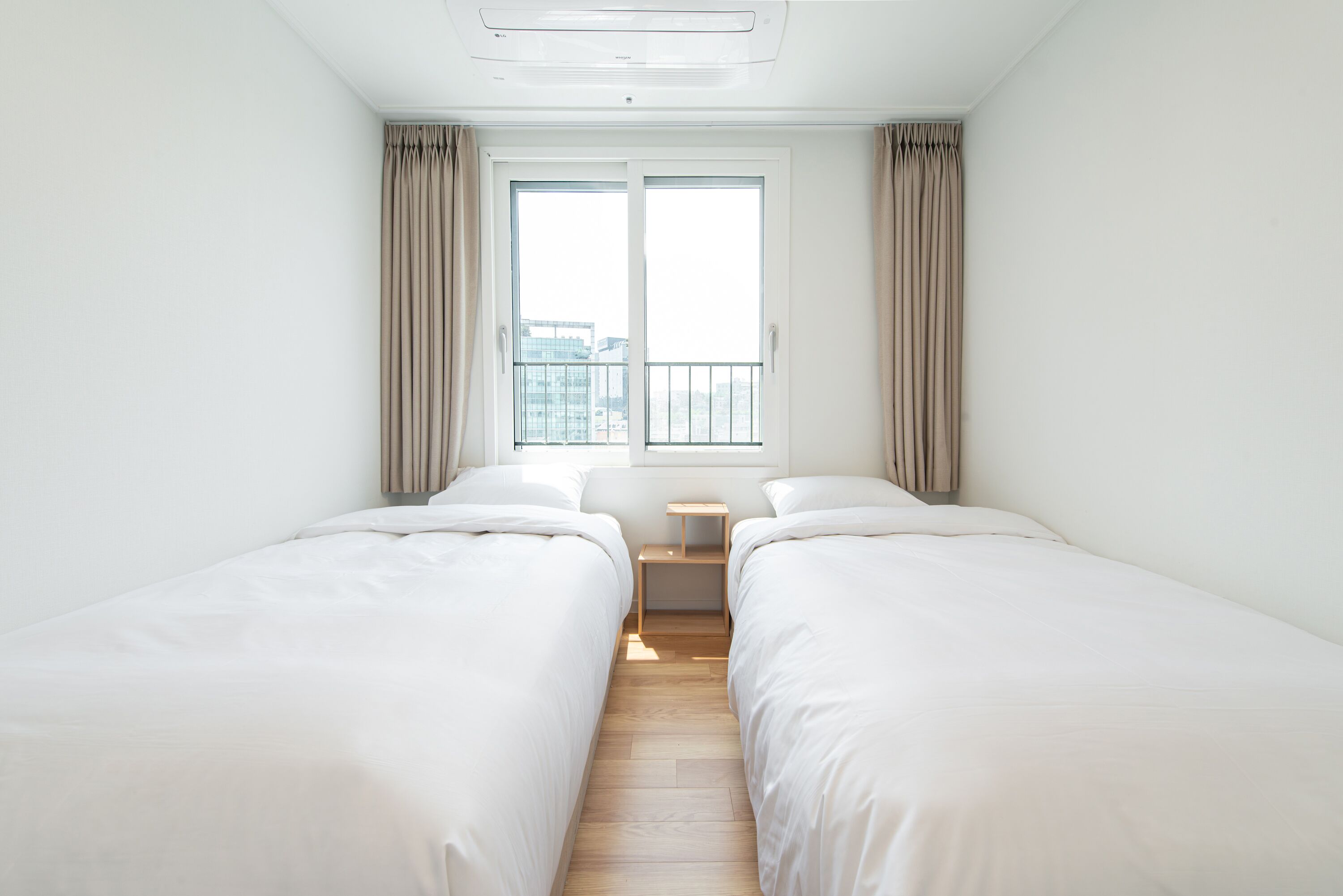 Quarto de hotel com duas camas de solteiro, uma pequena mesa de cabeceira, uma janela com cortinas e vista para a cidade.