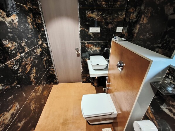 A bathroom with a marble wall, a wooden vanity, a white sink, and a toilet.