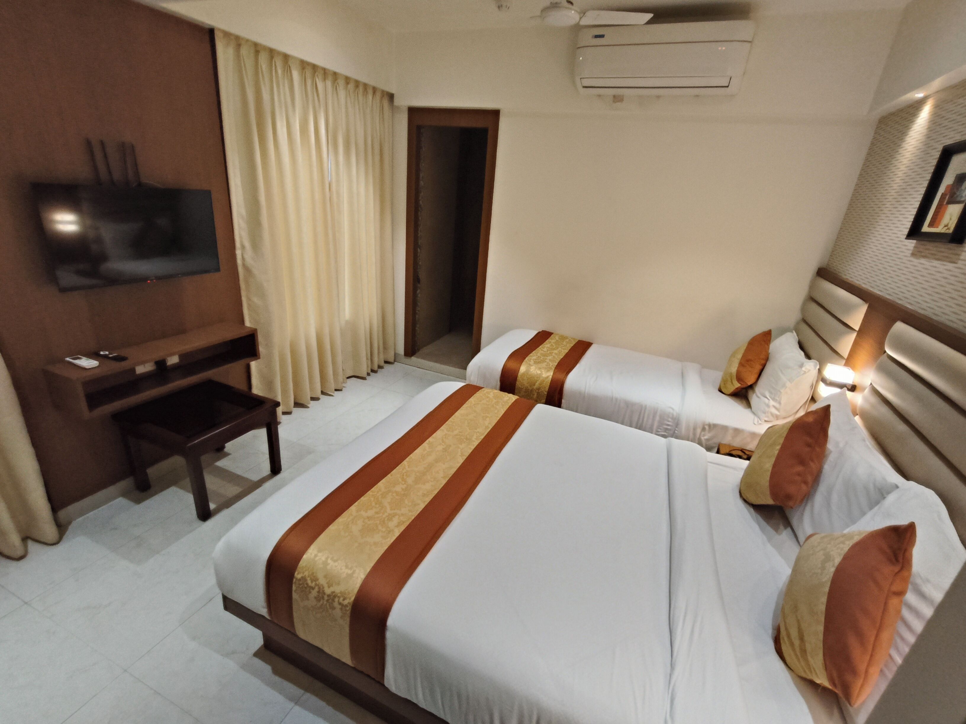 Ein Hotelzimmer mit zwei Betten, einem Schreibtisch, einem Fernseher und einer Klimaanlage.