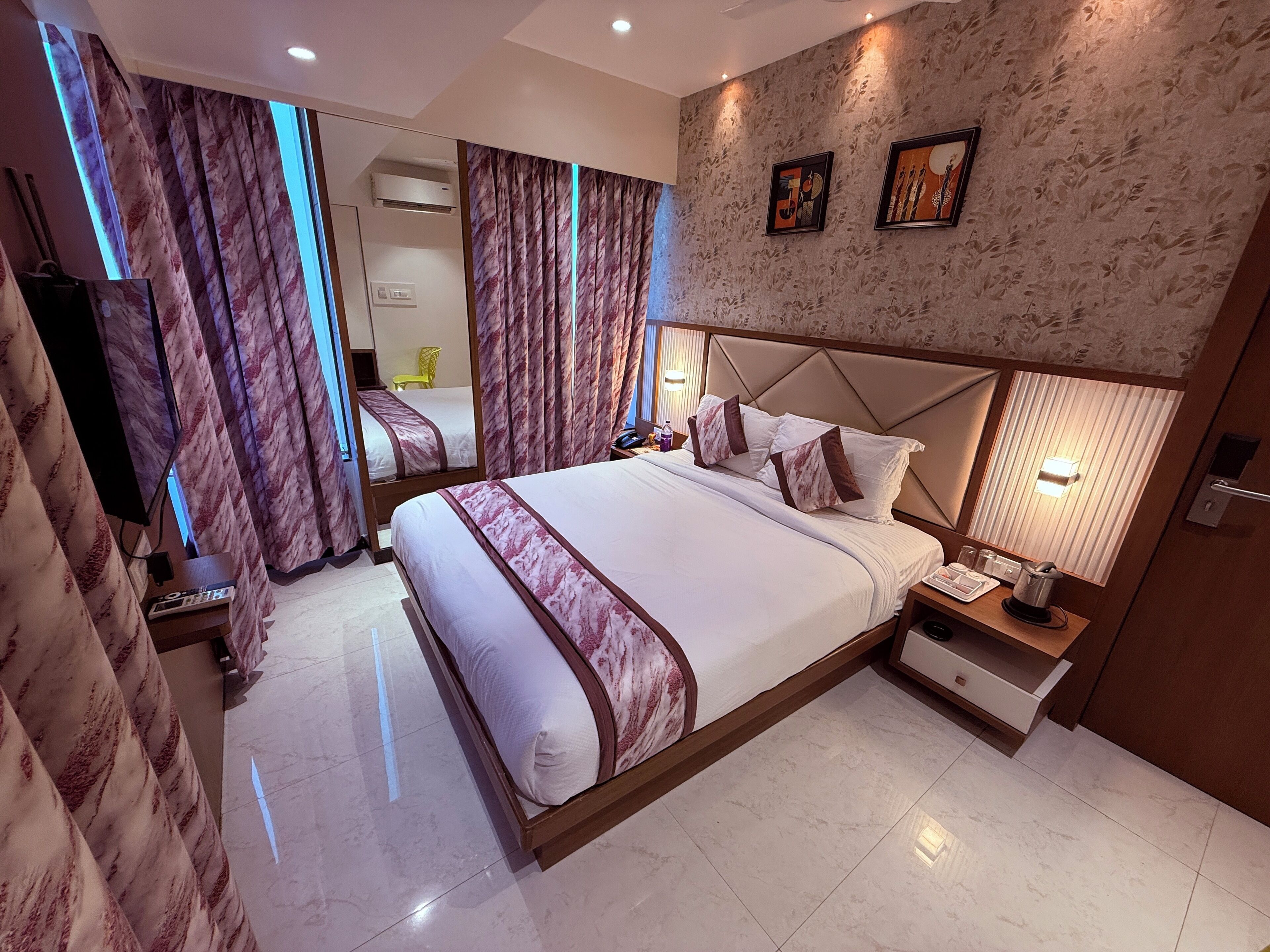 A modern hotel room with a large bed, a bedside table with a lamp, a mirror, and a wall-mounted air conditioner.