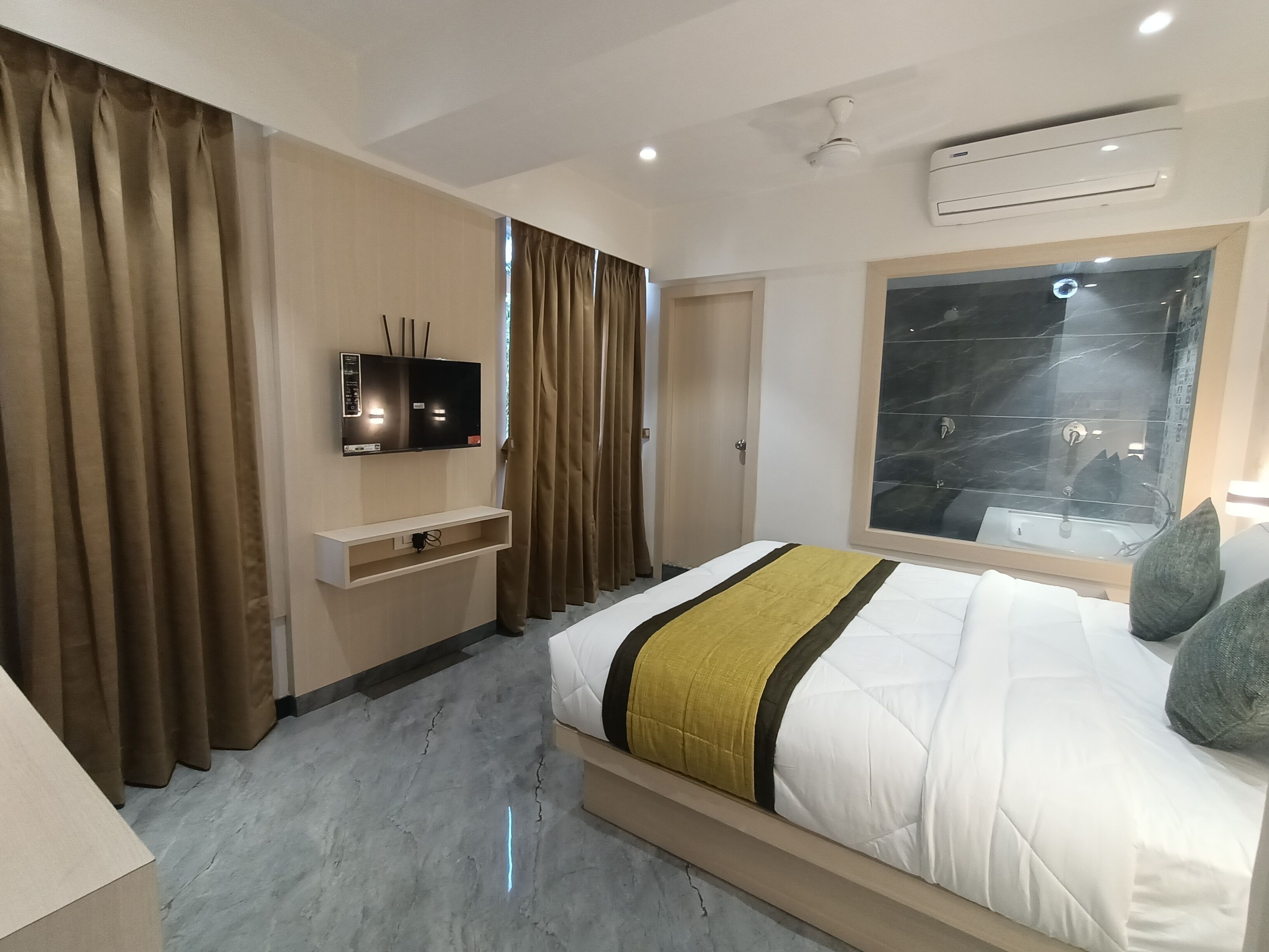 Een moderne hotelkamer met een groot bed, een aan de muur bevestigde televisie, een ingebouwde airconditioning en een badkamer met douchecabine.