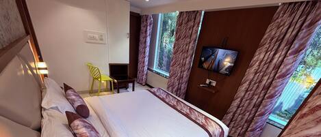 A hotel room with a large bed, a desk, a chair, a TV, and curtains.
