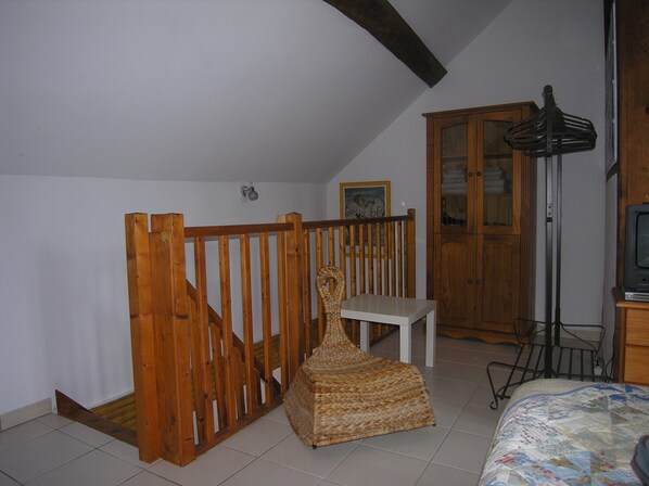 A room with a wooden staircase, a wicker chair, a white table, a wooden cabinet, and a television.