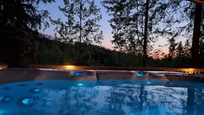Un bain à remous offrant une vue dégagée sur la forêt environnante et un coucher de soleil en toile de fond.