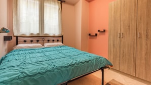 Ein Schlafzimmer mit einem Bett, einem Fenster mit Vorhängen, einem Kleiderschrank und einem kleinen Regal.