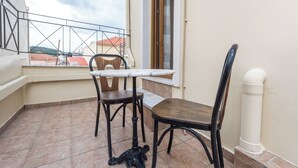 Ein Balkon mit Tisch und zwei Stühlen, ein Fenster mit Vorhängen und Blick auf Gebäude im Hintergrund.