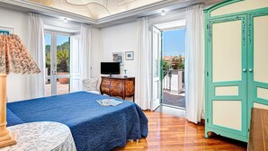 A bedroom with a bed, a TV, a dresser, and a door leading to a balcony.