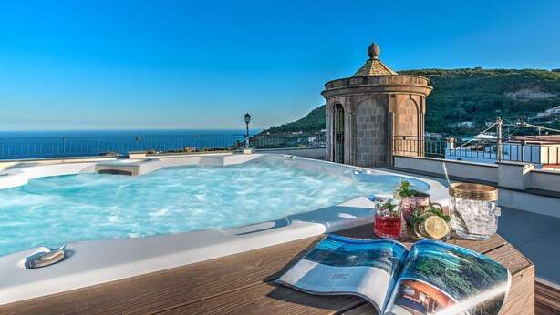 A hot tub on a deck with a view of the sea and a small tower structure.