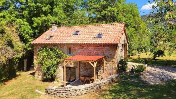 Une maison en pierre avec un toit en tuiles, un porche en bois et un mur de pierre qui entoure la propriété.