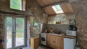 Une cuisine rustique avec des murs en pierre, des poutres en bois, une lucarne, une porte double donnant sur l’extérieur et des appareils électroménagers de base.