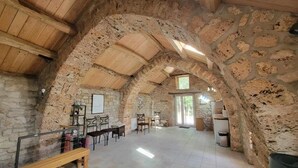 Un intérieur rustique en pierre, avec un haut plafond en bois, un coin repas et un banc.