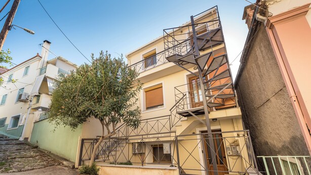 A multi-story building with a staircase leading to the upper floors, a tree in front, and a narrow street. - Mytilene Central Home 1 (Mitilini)