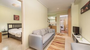 A compact living space with a bed, sofa, and a small table with a TV. A washing machine is visible in the background. - Mytilene Central Home 1 (Mitilini)