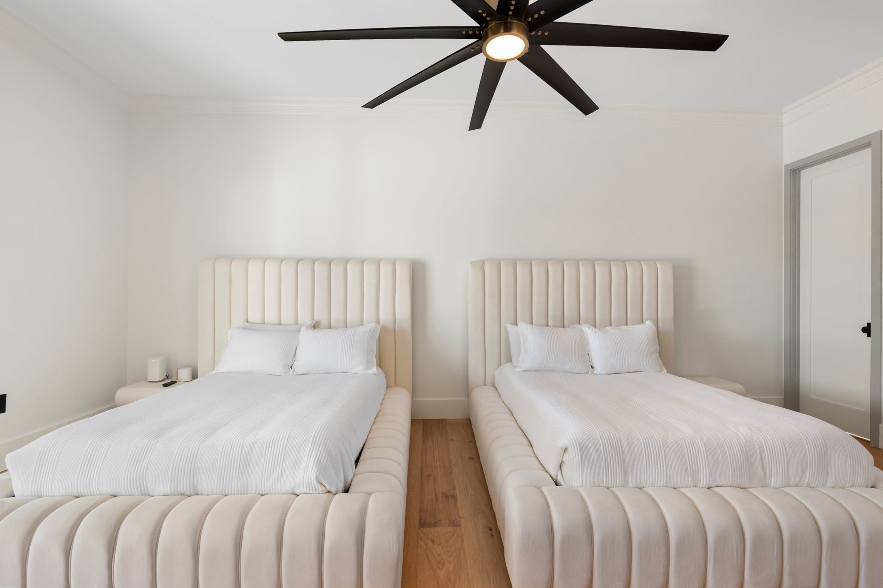 A bedroom with two beds, a ceiling fan, and a nightstand with a lamp.
