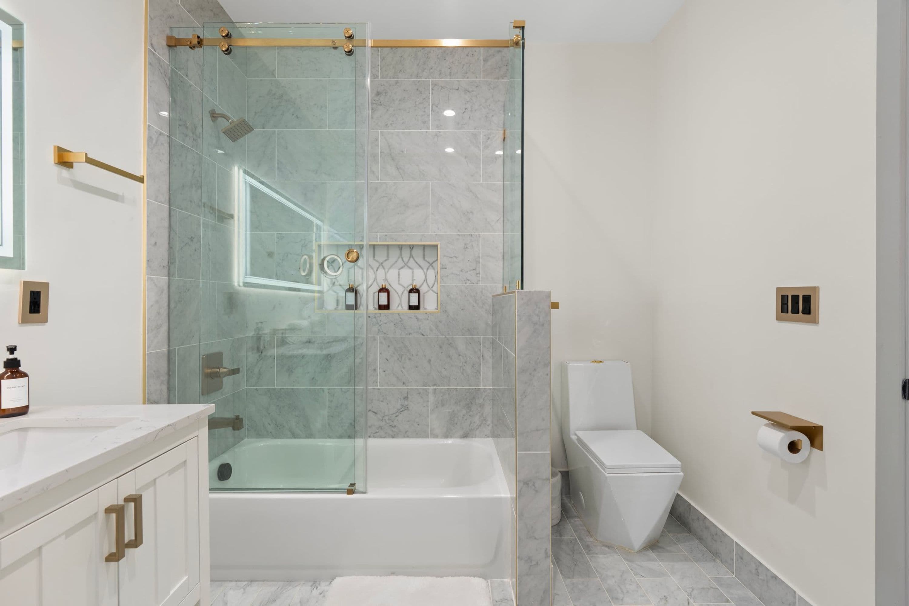 A modern bathroom with a glass-enclosed shower, a white bathtub, and a toilet.